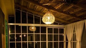 A cozy room with a sofa, a wooden chair, a small round table, and a large window with curtains. - Posada James (Xilitla)