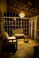 A cozy room with a sofa, a wooden chair, a small round table, and a large window with curtains.
