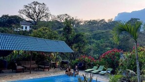 A swimming pool with lounge chairs and a covered seating area, surrounded by tropical vegetation and a mountainous backdrop. - Posada James (Xilitla)
