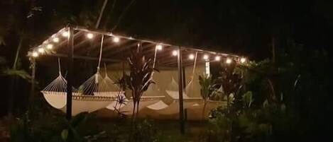 Un espacio al aire libre techado con luces colgantes, una hamaca y una estructura parecida a una tienda de campaña.
