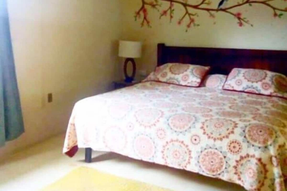 Un dormitorio con cama, mesita de noche, lámpara y un adorno en la pared.