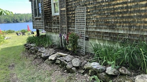 A wooden cabin with a stone wall and a view of a lake. - Lakefront cottage with privacy and charm! (Monson)