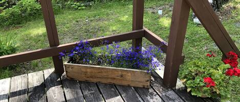 A wooden deck with a raised planter box containing blue flowers and a potted plant with red flowers.