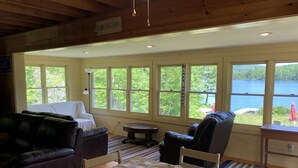 A cozy cabin interior with a large window overlooking a lake, furnished with a bed, a couch, and a dining table. - Lakefront cottage with privacy and charm! (Monson)
