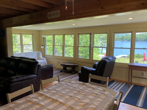 Interior acogedor de una cabaña con un ventanal grande que da a un lago, amoblada con una cama, un sofá y una mesa de comedor.