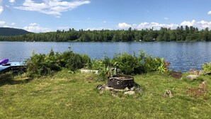 A lakeside camping area with a fire pit and a kayak. - Lakefront cottage with privacy and charm! (Monson)
