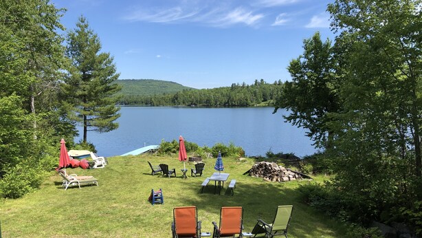A lakeside outdoor seating area with lawn chairs, umbrellas, and a boat. - Lakefront cottage with privacy and charm! (Monson)