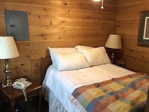 Una habitación de madera con una cama, dos lámparas de noche, un teléfono y una puerta.