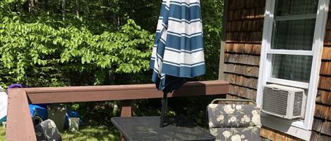 A wooden deck with a table and chairs, an umbrella, and a window with an air conditioning unit.
