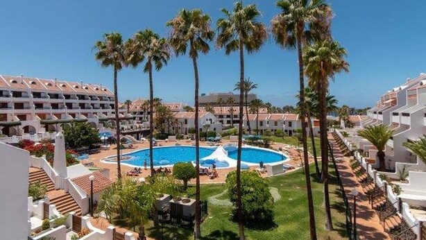 A resort with a central swimming pool, palm trees, and multiple-story buildings. - Parque Santiago II - 1 Bed (Playa de Las Americas)