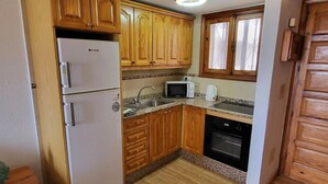 A compact kitchen with wooden cabinets, a white refrigerator, a microwave, a stove, and a sink. - Parque Santiago II - 1 Bed (Playa de Las Americas)