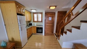 A kitchen with wooden cabinets, a refrigerator, and a microwave. There is a wooden staircase leading to another level. - Parque Santiago II - 1 Bed (Playa de Las Americas)