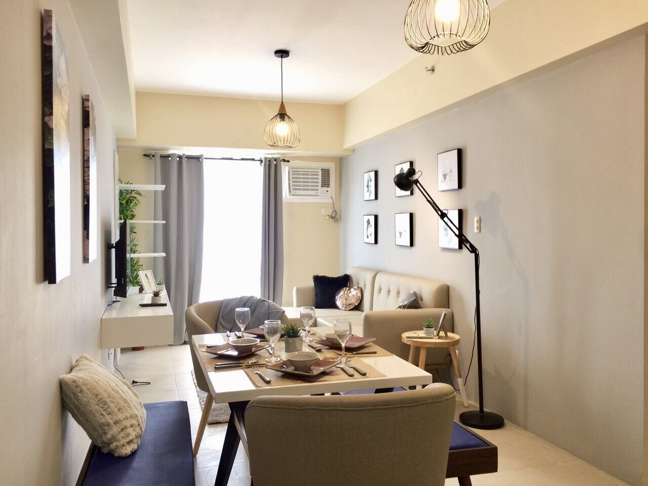 A modern living room with a dining table set for four, a sofa, a floor lamp, and a TV on a stand.
