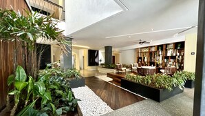 A spacious lobby with a wooden floor, a seating area with chairs, a bookshelf, and indoor plants. - Pavilion Paradise - Steps away from everything! (Puerto Vallarta)