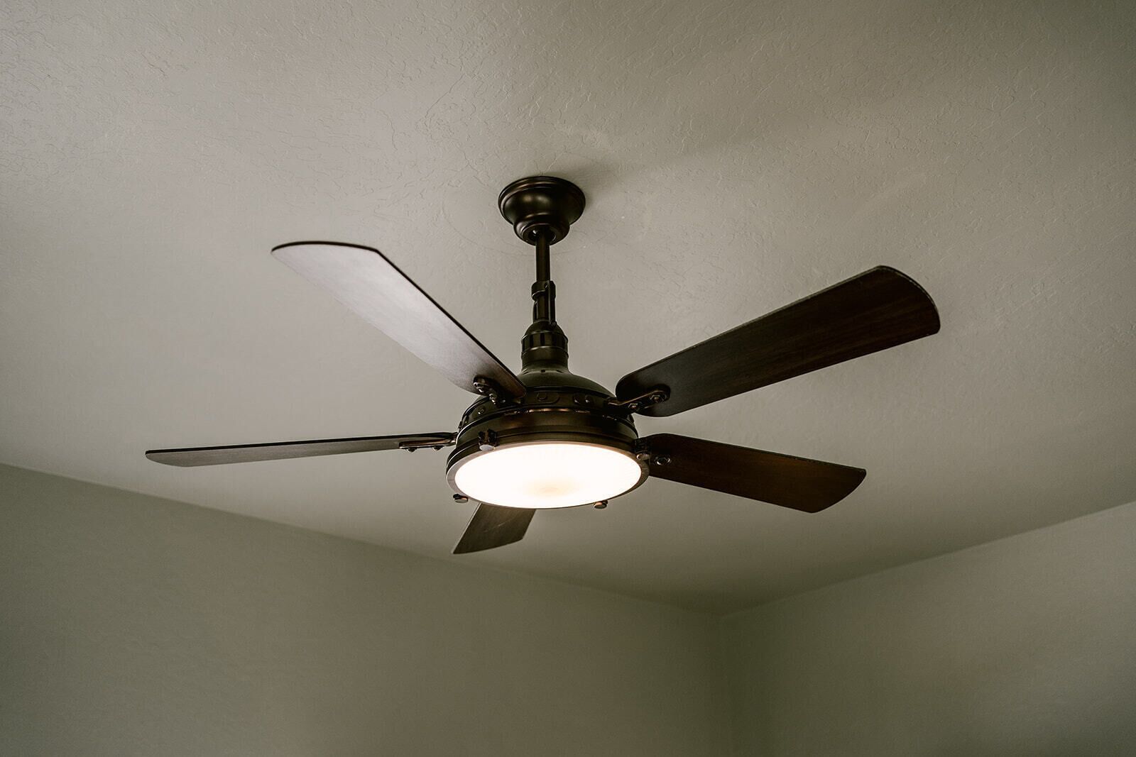 Un ventilador de techo con cuatro aspas y una lámpara en una habitación con paredes lisas.