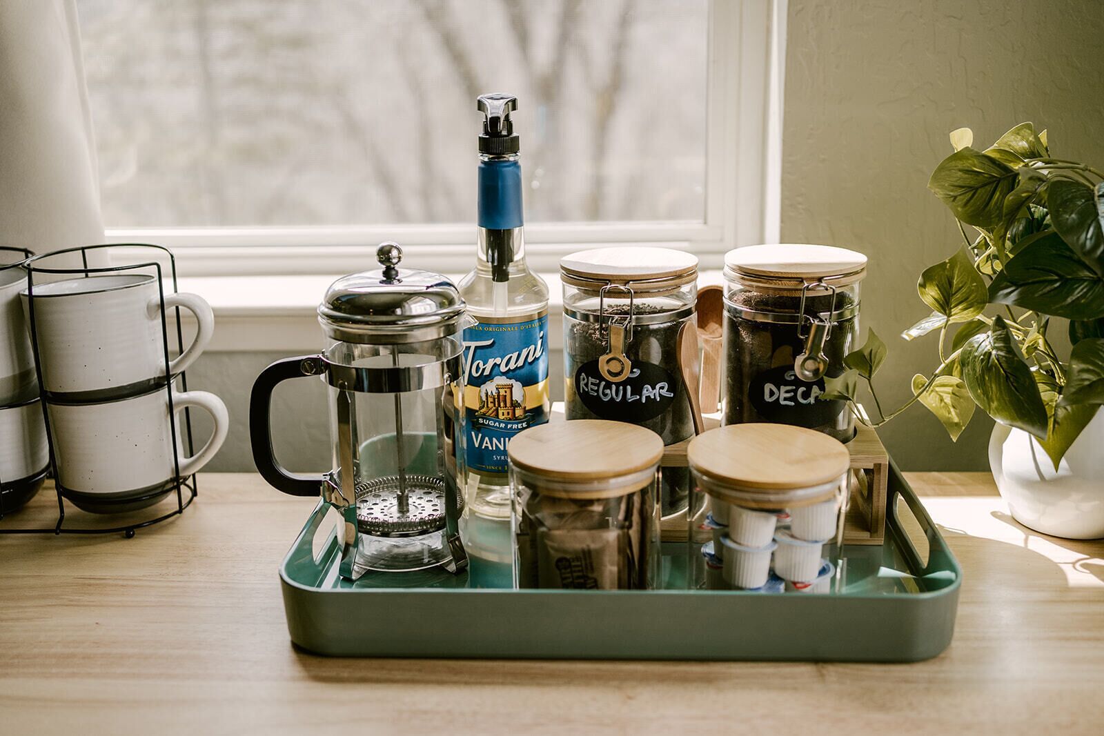 Een aanrecht met een koffiezetapparaat, een fles Torani, en twee potten met de aanduiding 'Normaal' en 'Koffieloos'.