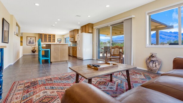 A spacious living area with a large window, a kitchen with wooden cabinets, and a dining area with a blue chair. - Incredible VIEWS, pool, spa, ping pong table, by GOLF course, bike and walk path (Tucson)