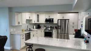 Una cocina moderna con armarios blancos, electrodomésticos de acero inoxidable, encimera de granito y taburetes de bar.