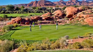 Campo de golf con jugadores, rodeado de formaciones rocosas rojas y casas.