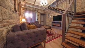 A living room with a fireplace, a sofa, a television, and a wooden staircase. - Orion Adatepe (Ayvacik)