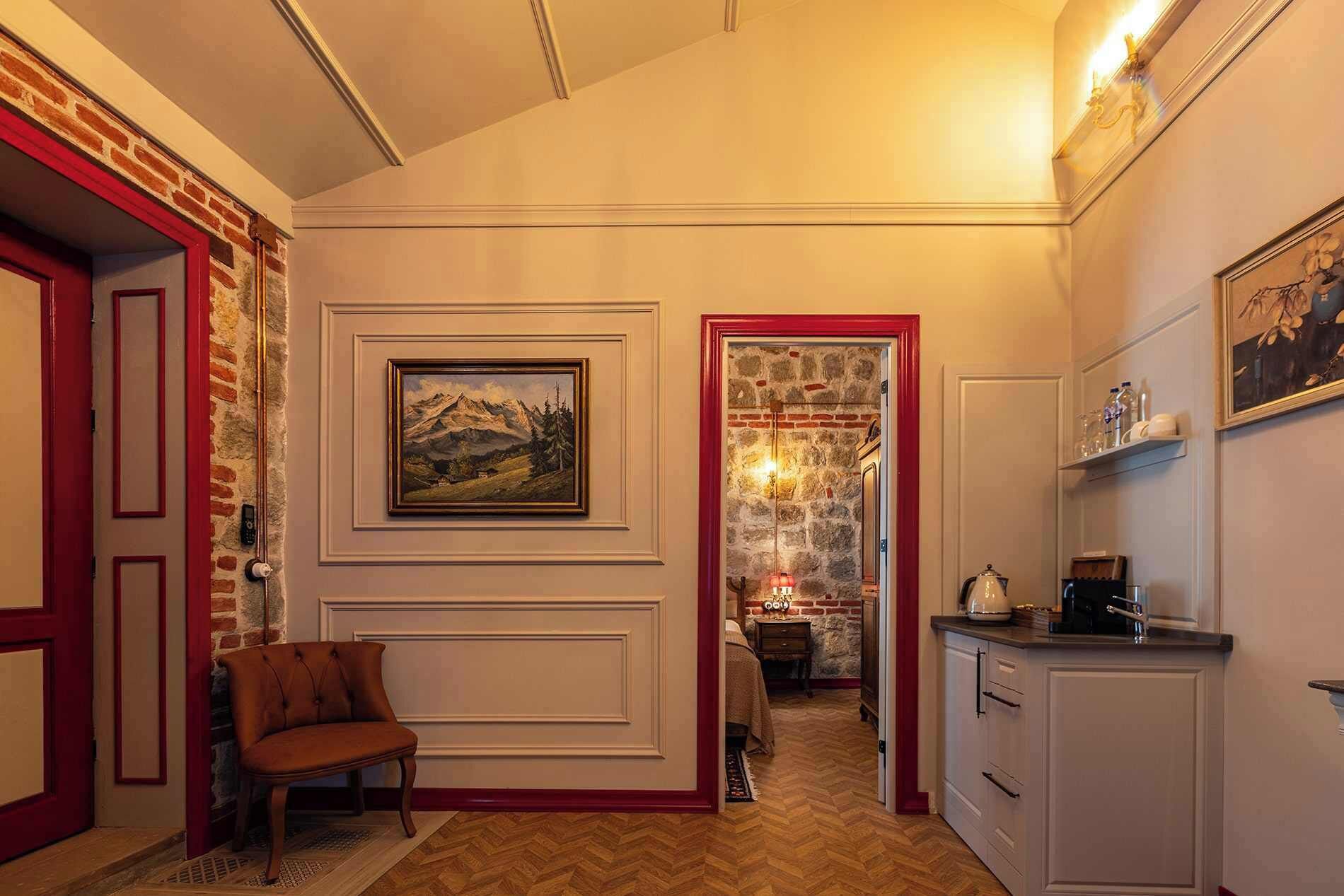 A hallway with a wooden chair, a framed painting, and a kitchen area with cabinets and a countertop.
