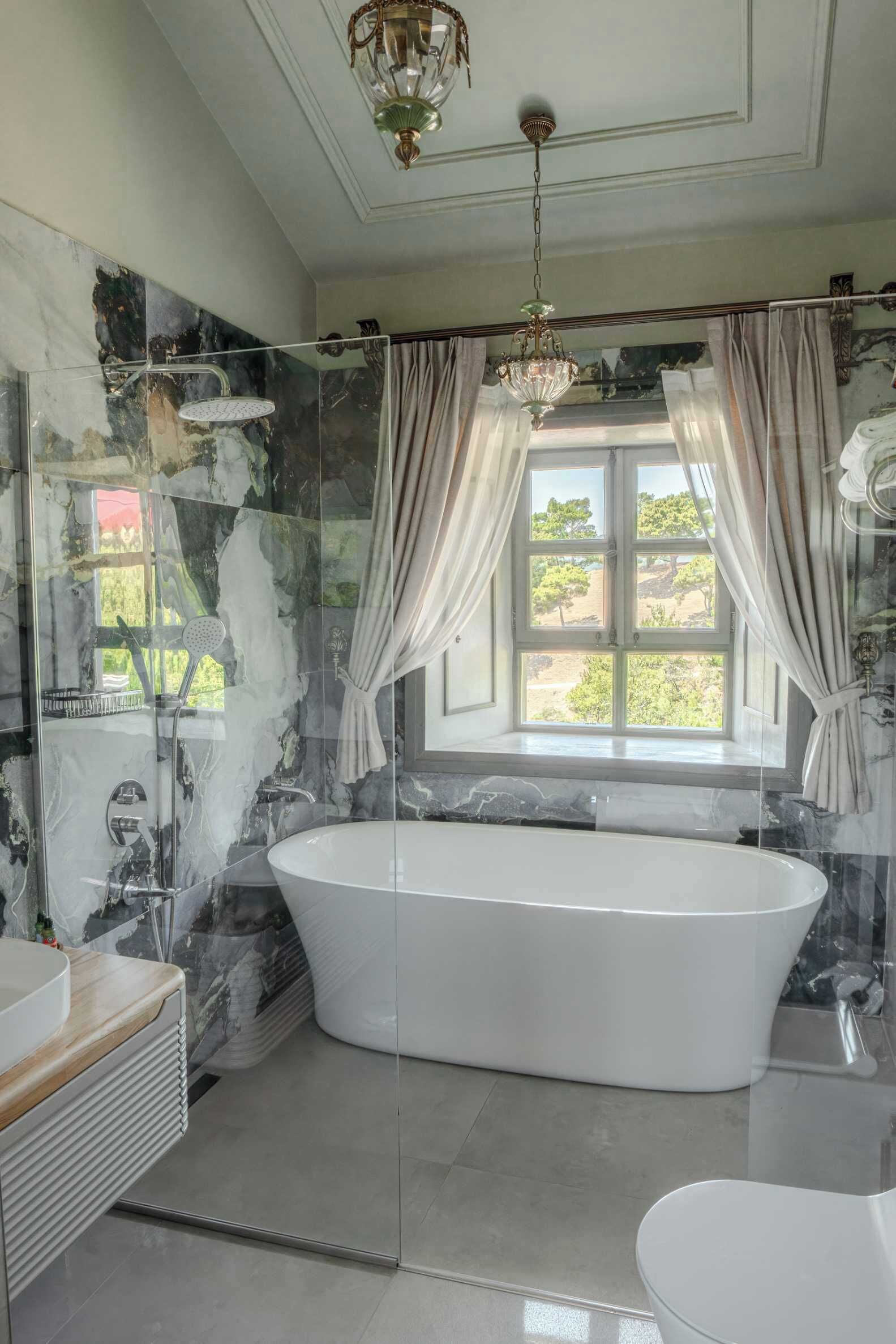 A bathroom with a freestanding bathtub, a glass-enclosed shower, and a window with curtains.