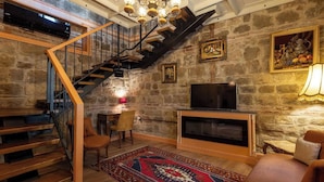 A cozy living room with a stone wall, a wooden staircase, a TV, and a patterned rug. - Orion Adatepe (Ayvacik)
