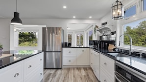 Una cocina moderna con electrodomésticos de acero inoxidable, armarios blancos y encimera negra.