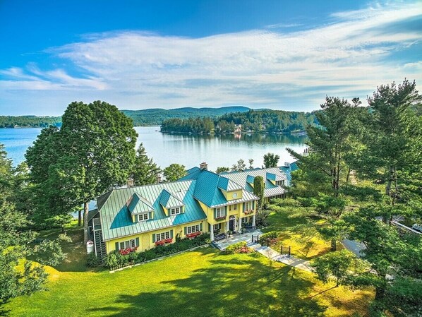 A large, multi-story building with a green roof, surrounded by lush greenery and a lake.