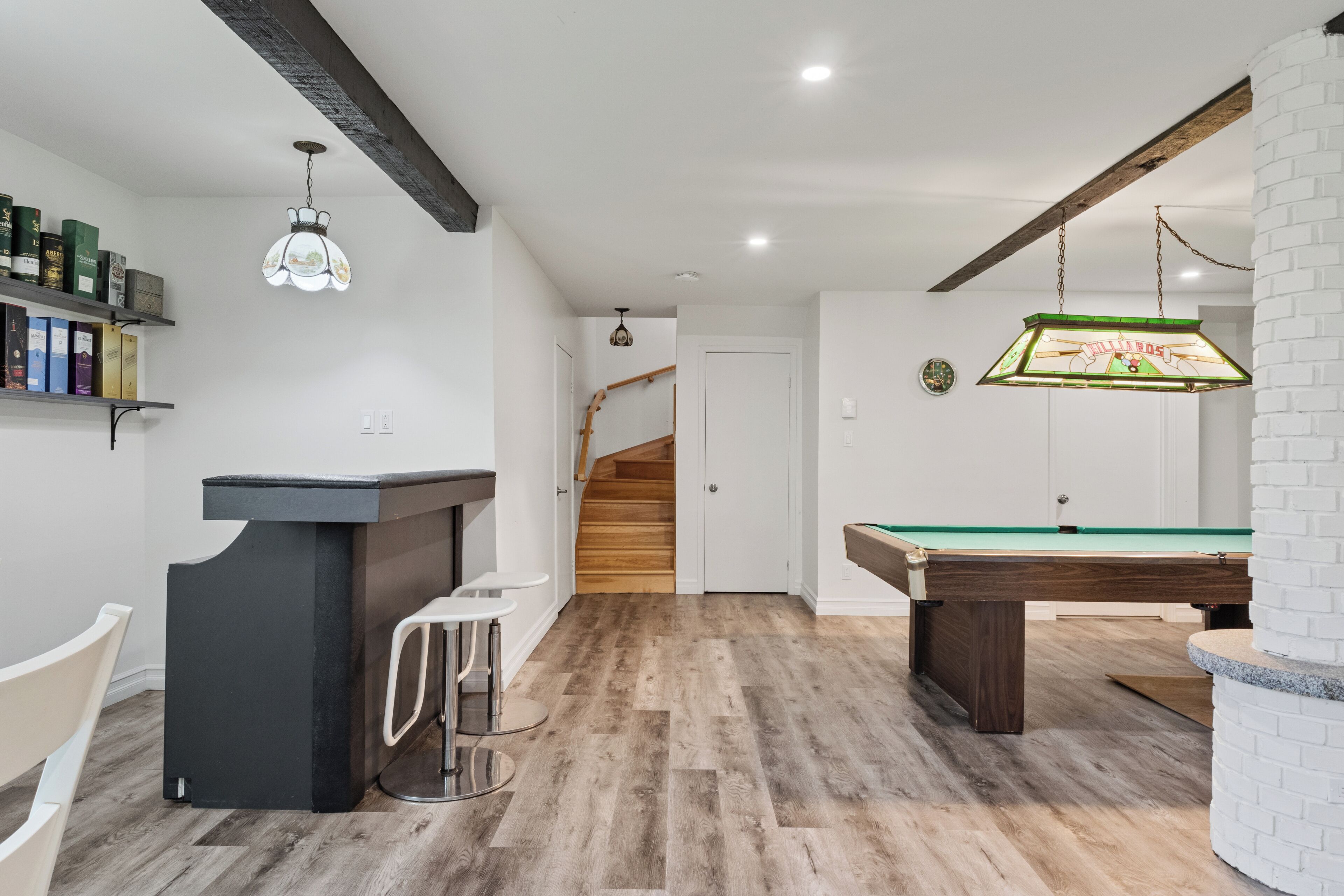 Une pièce équipée d’une table de billard, d’un coin bar et d’un escalier menant à un autre niveau.