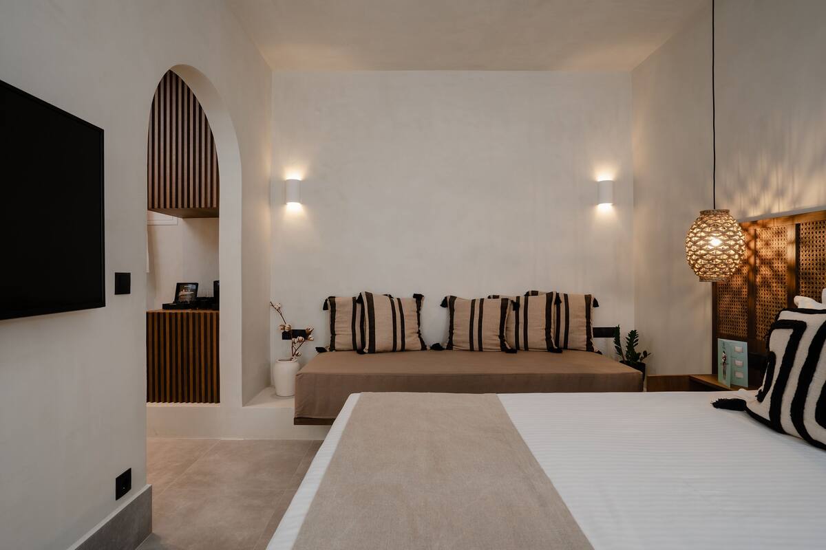 Een moderne slaapkamer met een groot bed, een zithoek met kussens, een televisie en een decoratieve lamp.