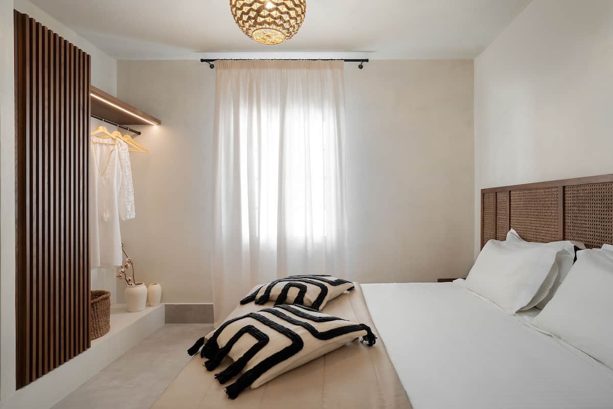 Een moderne slaapkamer met een bed, kussens, een hanglamp, een raam met dunne gordijnen en een houten hoofdbord.