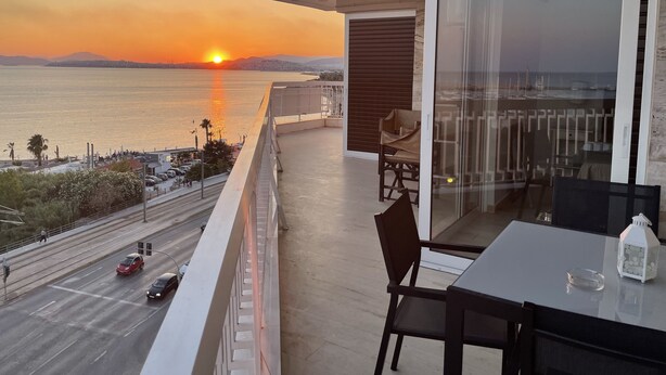 Een balkon met uitzicht op de zonsondergang boven de zee, een tafel met stoelen en een glazen deur.