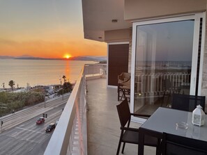 A balcony with a view of the sunset over the sea, a table with chairs, and a glass door. - Athens Edem Beach Penthouse, panoramic sea view (Alimos)