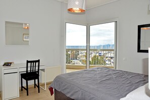 A bedroom with a bed, a desk, a chair, a window with a city view, and a hanging light fixture. - Athens Edem Beach Penthouse, panoramic sea view (Alimos)