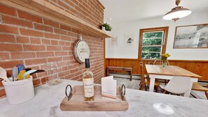 A kitchen with a brick wall, wooden shelves, a clock, and a wooden table with chairs. - Peaceful Mountain Retreat Near Appalachian Trail, Wineries, Breweries and More (Bluemont)