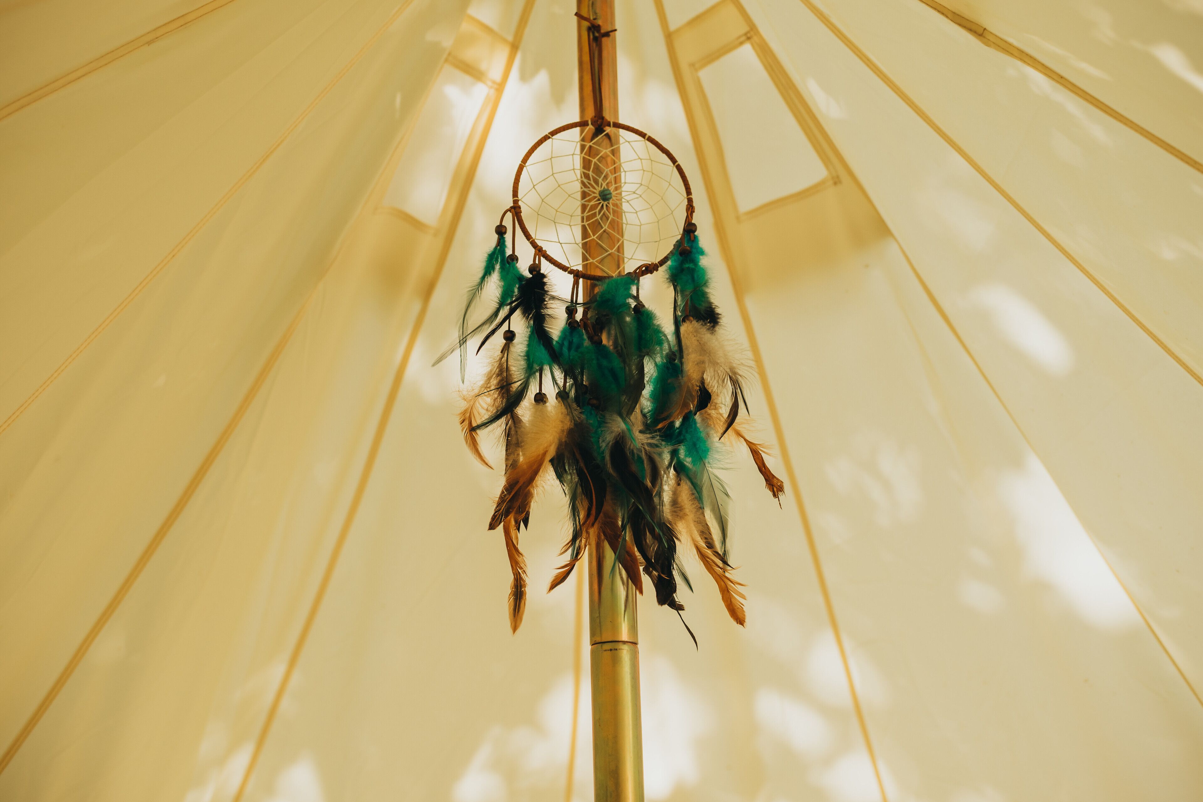A dreamcatcher hanging from a pole in a room with a high ceiling and vertical beams.