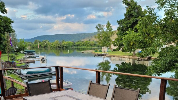 Una terraza con mesa y sillas que da a un lago con barcos y vegetación.