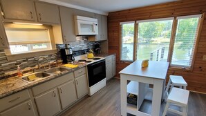 Una cocina con microondas, estufa, lavaplatos y una ventana con persianas.