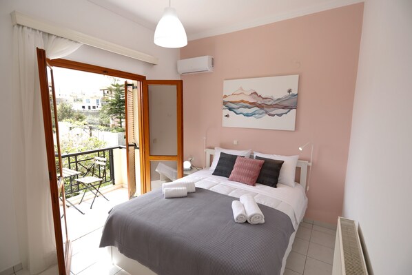 Ein Schlafzimmer mit Bett, einem Gemälde, einem Balkon mit Stuhl und einer Klimaanlage.