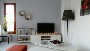 Un soggiorno moderno con una TV a schermo piatto su un mobile bianco, un poggiapiedi rosso e una lampada da terra.