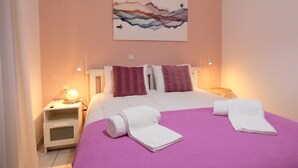 Camera da letto con un letto, cuscini, un comodino, una lampada e un quadro appeso al muro.