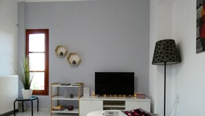 Un soggiorno moderno con una TV a schermo piatto, un tavolino da caffè bianco, un poggiapiedi rosso, una lampada da terra e una finestra con vista.