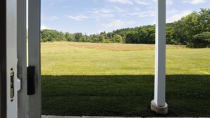A view from a covered porch overlooking a grassy field with trees in the background.