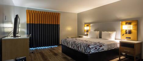 A hotel room with a bed, bedside tables, a desk with a computer, and a window with curtains.