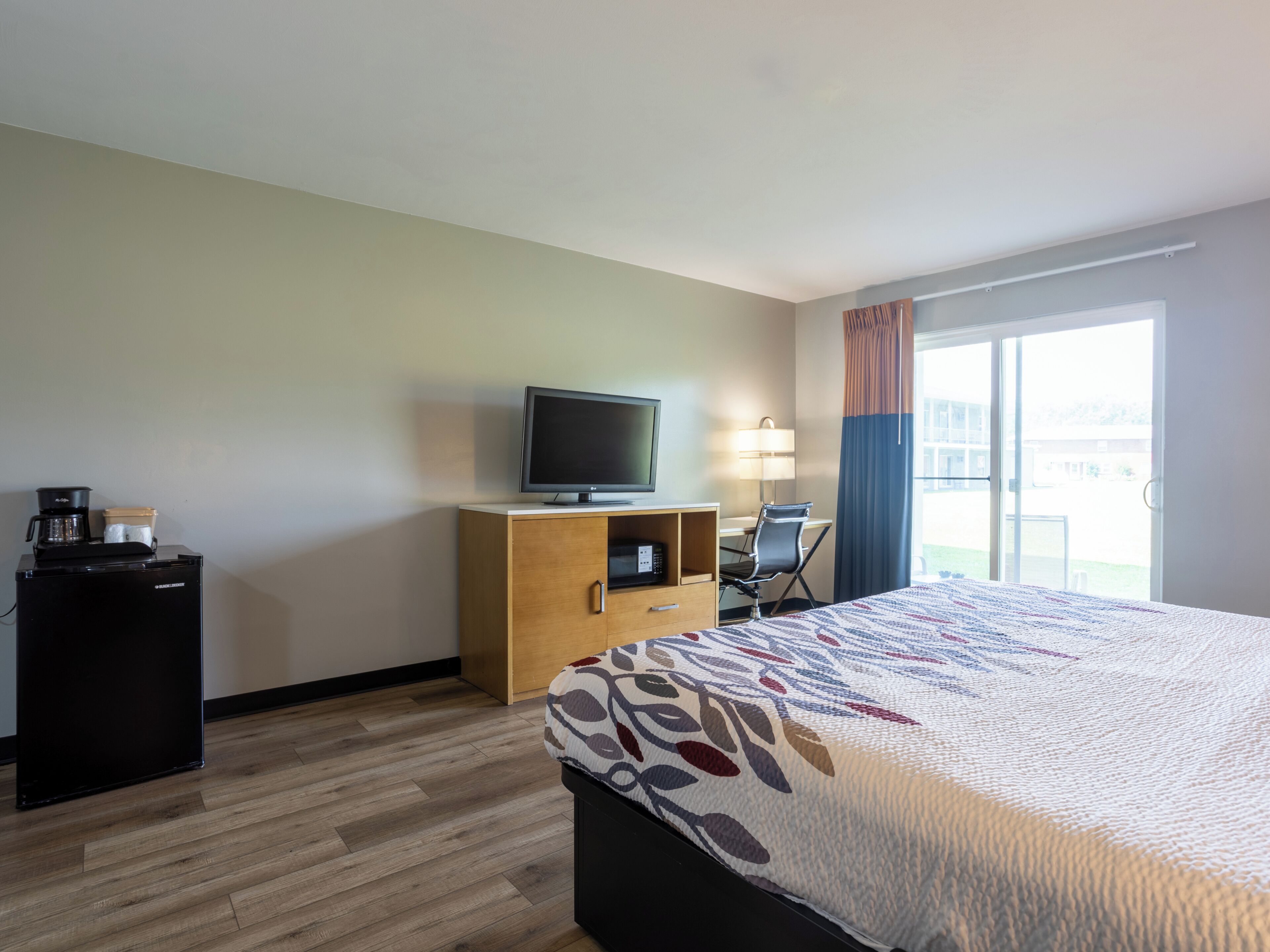 A hotel room with a bed, a desk with a computer, a television, and a coffee machine.