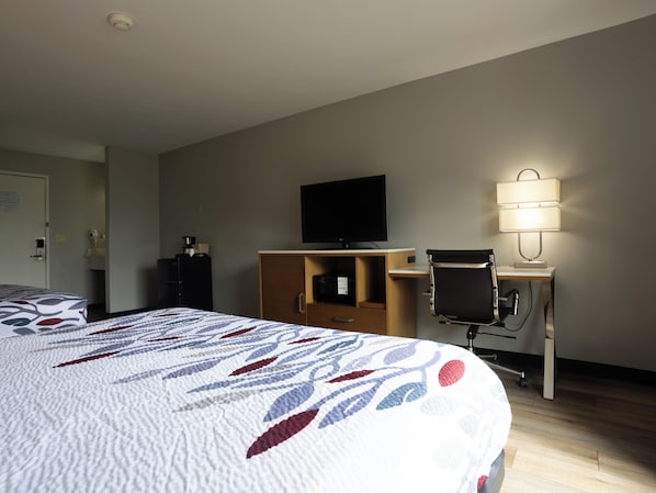 A hotel room with a bed, a desk, a television, a lamp, and a wardrobe.