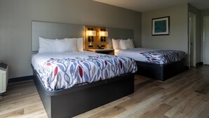 A hotel room with two beds, a bedside table with lamps, a framed picture on the wall, and a wooden floor.