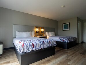 Habitación de hotel con dos camas, una mesita de noche con lámparas, un cuadro en la pared y suelo de madera.