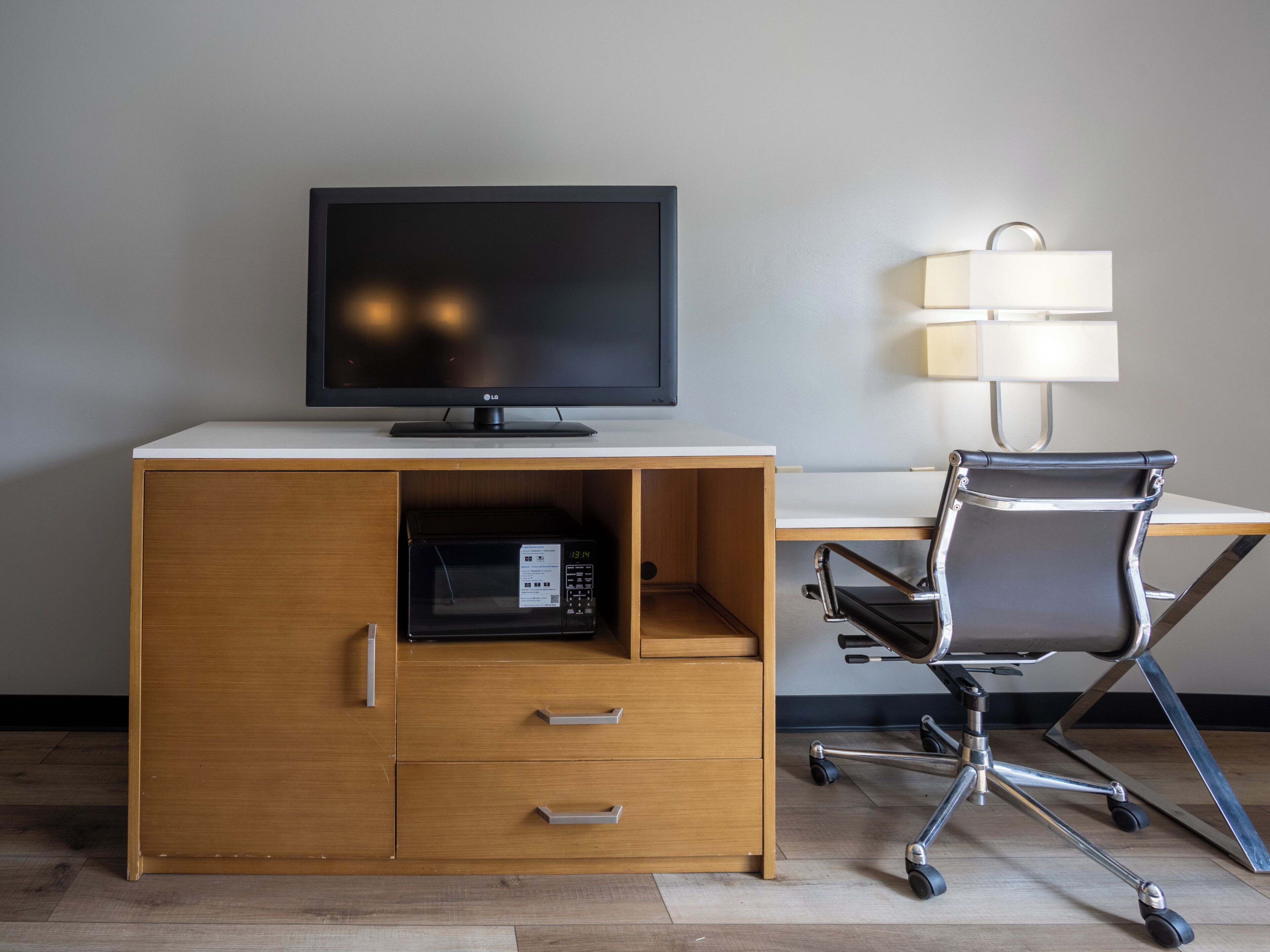 Un espace de travail moderne avec un bureau en bois, un écran noir, un four à micro-ondes et une chaise de bureau noire.